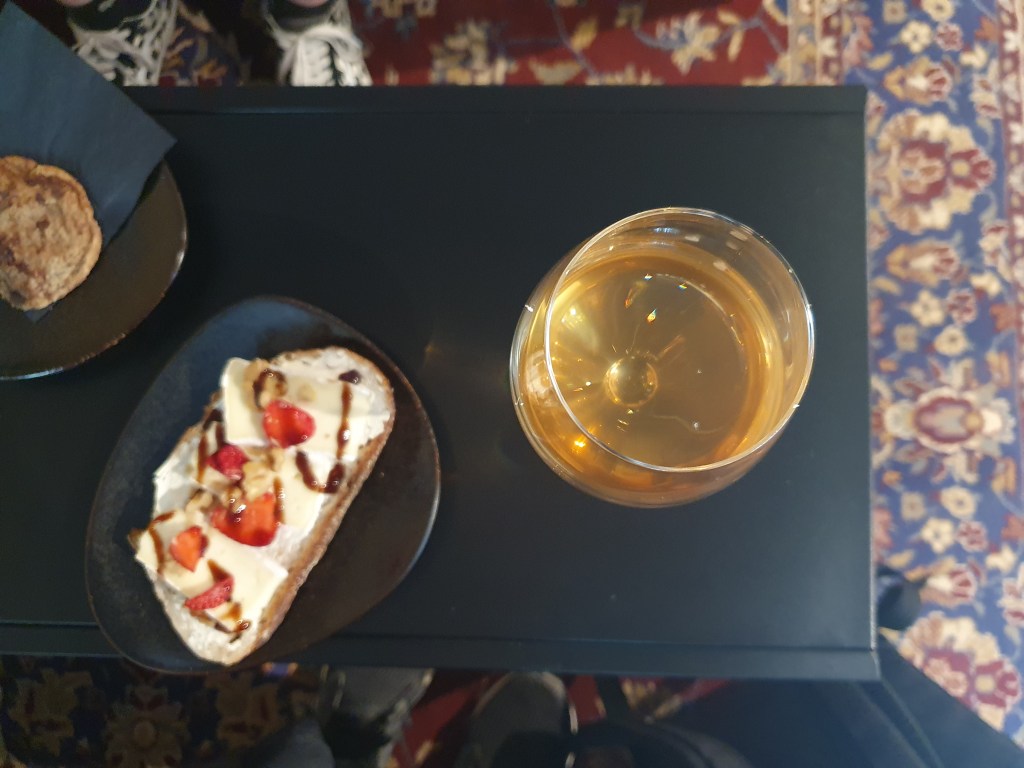 Kahiwa Coffee & Wine pöydällä lasillinen natuviiniä ja juurileipä brie-juustolla ja mansikoilla.